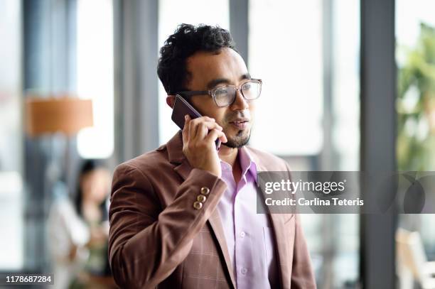 malay man working on a smart phone in a bright office - handsome muslim men stock pictures, royalty-free photos & images