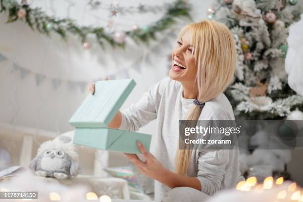 happy woman in pajamas holding gift by the christmas tree - beautiful woman christmas stock pictures, royalty-free photos & images