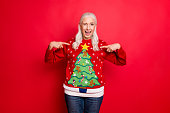 I like my jumper concept. Photo of blinking grey-haired positive hinting cheerful nice granny showing you her best with small pompons gingerbread men decor pullover isolated bright color background