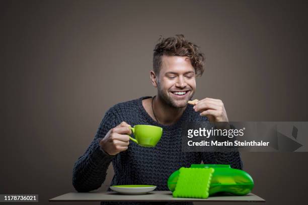 junger smarter mann trinkt kaffee und isst kekse - mann kaffee 個照片及圖片檔