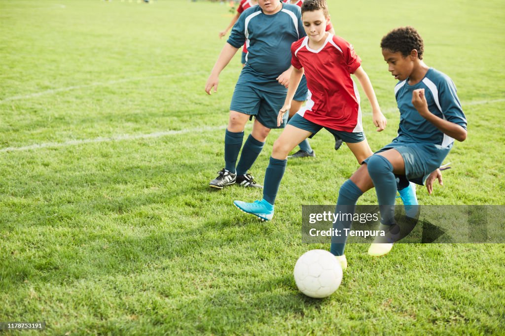 Adolescente dribla seus adversários durante um jogo de futebol.