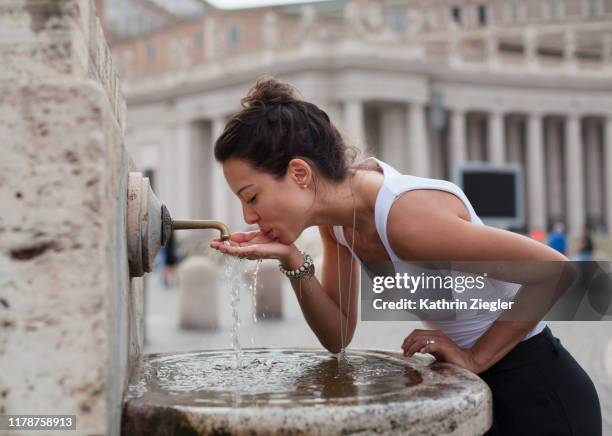 woman drinking water from fountain at st. peter's square, rome, italy - wasserstrahl stock-fotos und bilder