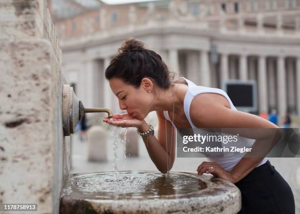 woman drinking water from fountain at st. peter's square, rome, italy - water fountain stock pictures, royalty-free photos & images