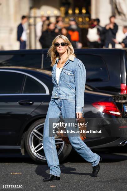 Camille Charrière wears earrings, sunglasses, a white top, a washed-out light blue denim jacket with a cream-color fluffy collar, washed out light...