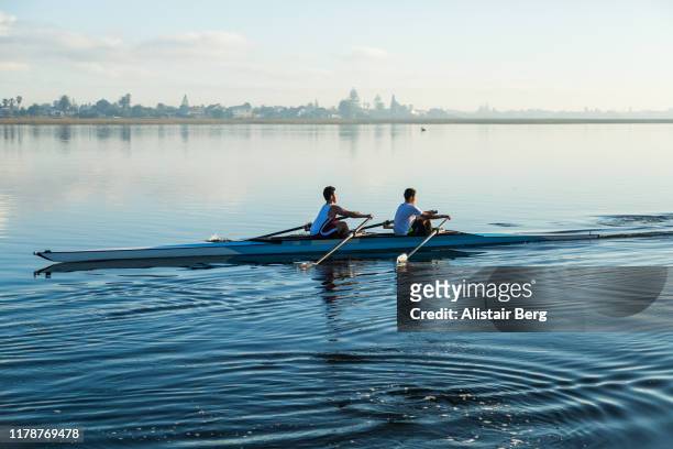 pair of mixed race rowers sculling on lake at dawn - match sport stockfoto's en -beelden