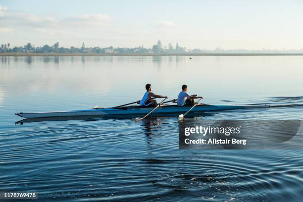 pair of mixed race rowers sculling on lake at dawn - rowing competition stock pictures, royalty-free photos & images