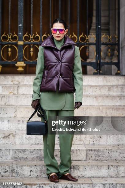 Doina Ciobanu wears earrings, sunglasses, an almond-green jacket, almond-green full-length pants, a dark brown puffer vest, dark brown gloves with...