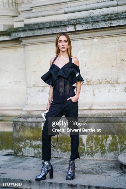 Model Teddy Quinlivan wears a black lace mesh ruffled off-shoulder top, black pants, silver shiny glitter shoes with high heels, outside Louis...