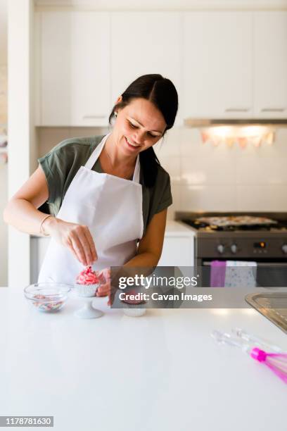 a baker woman smiling as she decorates a pink cupcake - decorar um bolo imagens e fotografias de stock