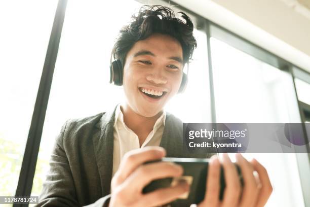 young man is enjoying new mobile app - asian cinema stock pictures, royalty-free photos & images