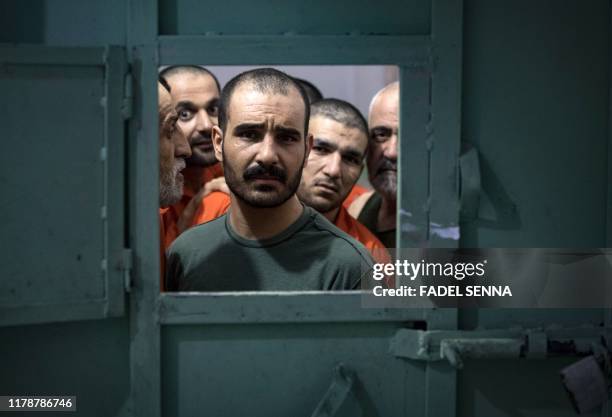 Men, suspected of being affiliated with the Islamic State group, look out of the opening of a prison cell in the northeastern Syrian city of Hasakeh...