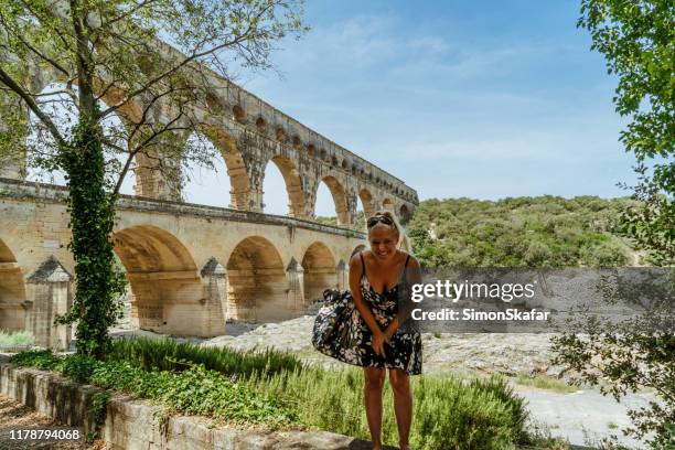 woman standing against aqueduct bridge and smiling at camera, vers-pont-du-gard, gard, france - pont du gard aqueduct stock pictures, royalty-free photos & images