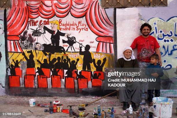 Picture taken on October 28 shows Syrian artist Aziz al-Asmar posing with relatives near a mural he painted in the town of Binnish in the...