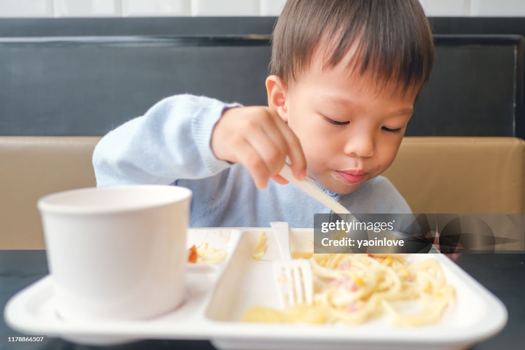 Asian 3 - 4 years old toddler boy toddler boy child eating spaghetti with spoon and fork for lunch at home, in restaurant, Yummy toddler food