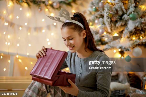 teenager-mädchen in pyjamas und geweih stirnband eröffnung weihnachtsgeschenk - geschenk auspacken stock-fotos und bilder