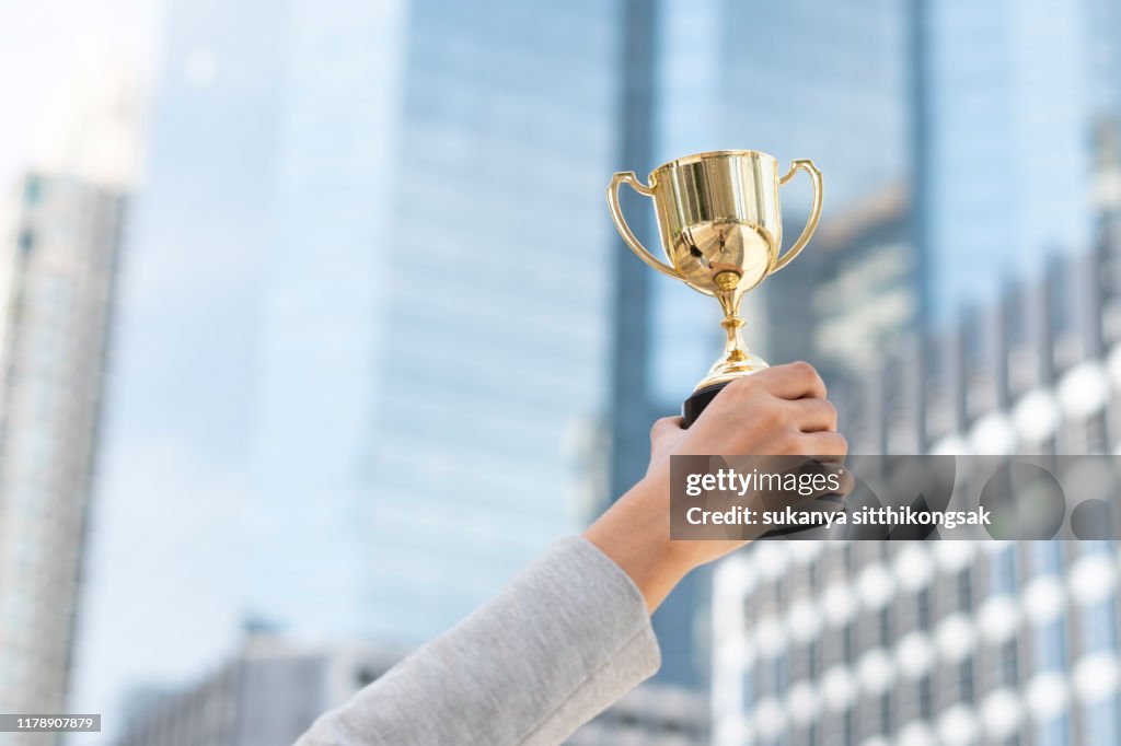 Business goals,Business concept.Close up hand of businesswoman holding gold trophy.