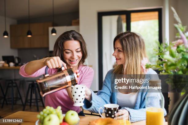 front view portrait of mature mother with adult daughter sitting at home, pouring coffee. - coffee plunger stock pictures, royalty-free photos & images