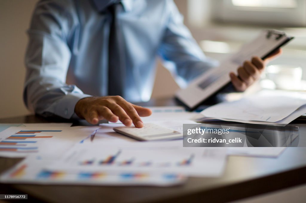 Concept de comptabilité d'affaires, homme d'affaires utilisant la calculatrice avec l'ordinateur portable, le budget et le papier de prêt dans le bureau.