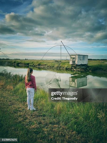 girl standing by a river looking at fishing huts and nets, rue du gois causeway, noimoutier island, vendee, france - vendée photos et images de collection