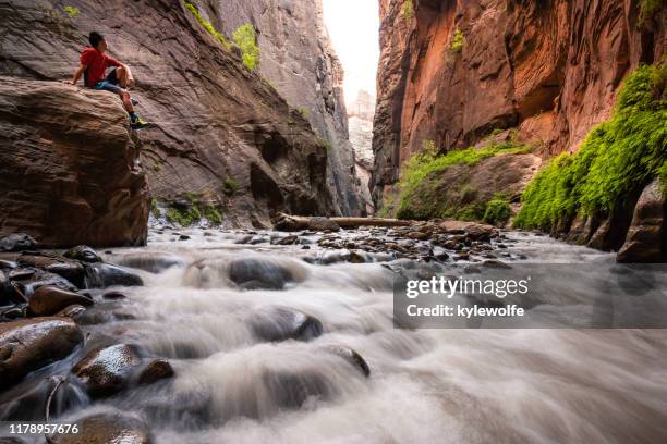 hiker sitting on a boulder in slot canyon, the narrows, zion national park, utah, united states - estrechos de zion fotografías e imágenes de stock