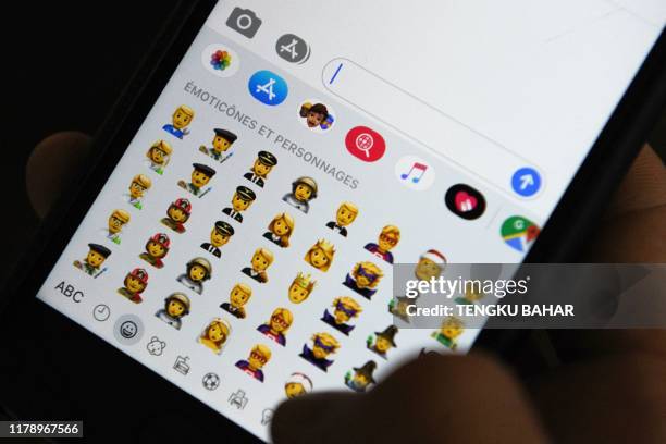 Person holds an iPhone showing emojis in Hong Kong, on October 30, 2019. - Apple has put out new gender neutral emojis of most of its people icons --...