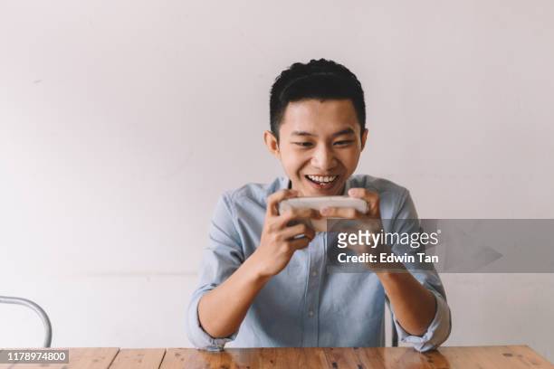 昼休みの間にカフェでオンラインゲームをしているアジアの中国人男性 - マッチ ストックフォトと画像