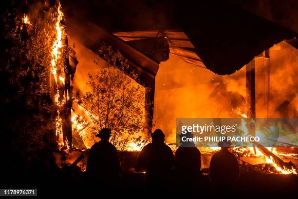 Firefighters look on as a structure burns during the Kincade fire off Highway 128, east of Healdsburg, California on October 29, 2019. California...