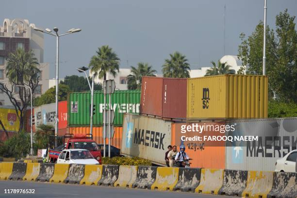 Commuters ride past shipping containers placed on a road in Islamabad on October 30 to seal off the city's diplomatic enclave ahead of an...