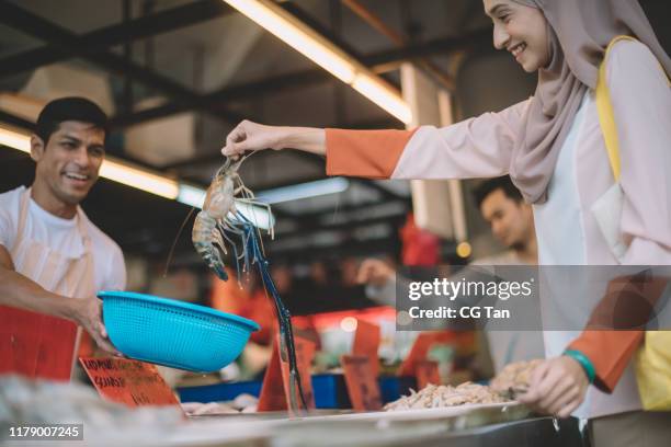 an asian malay female pick up a tiger prawn and putting it into the basket given by fish stall vendor in wet market - wet market stock pictures, royalty-free photos & images