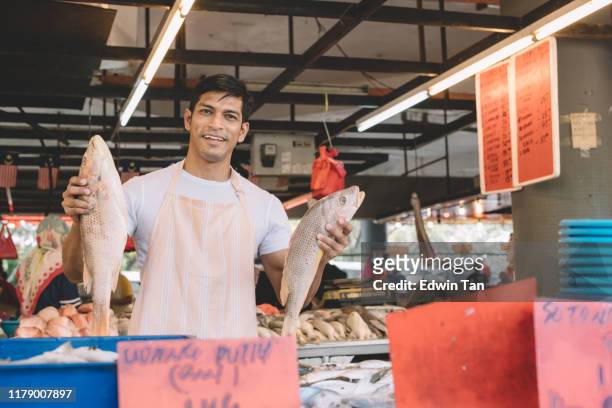 een viskraam eigenaar die vissen op zijn hand kijkt naar camera glimlachend voor zijn kraam - fish market stockfoto's en -beelden