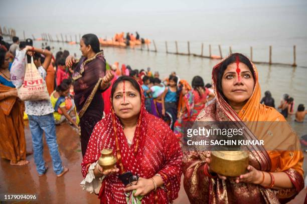 Women holding jars look on as devotees take bath early in the morning in the Ganges river and bring holy water to their home to prepare offerings on...