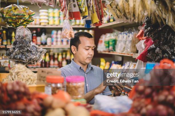 un adulto medio malaya asiático calculando el costo de los artículos seleccionados de su cliente - tienda de especias puesto de mercado fotografías e imágenes de stock
