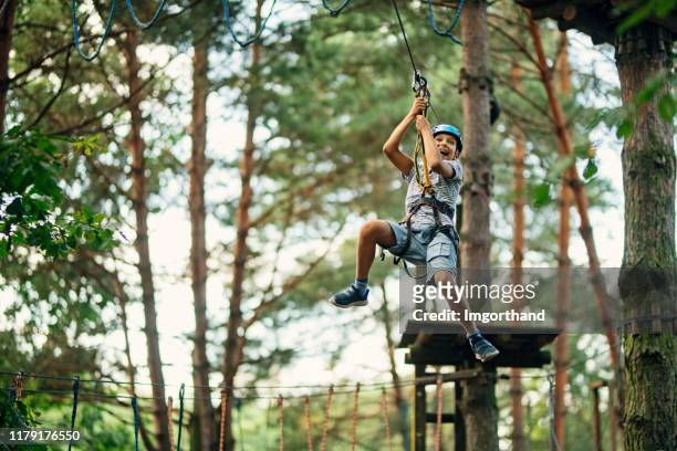 pequeño niño ziplining en el bosque - zip line fotografías e imágenes de stock