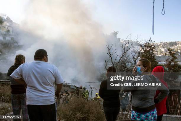 Locals look at firefighters working to extinguish a fire affecting two houses on a hillside at Camino Verde neighborhood in Tijuana, Baja California...