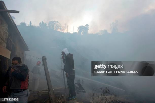 Residents cover from the smoke work to extinguish a fire affecting two houses on a hillside at Camino Verde neighborhood in Tijuana, Baja California...