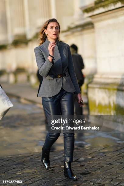 Guest wears a gray jacket and a Vuitton belt, black leather pants, black shiny shoes, earrings, outside Louis Vuitton, during Paris Fashion Week -...