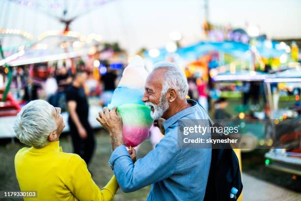 couples mûrs joyeux parlant tout en mangeant la barbe à papa au parc d'attractions. - parc dattractions photos et images de collection