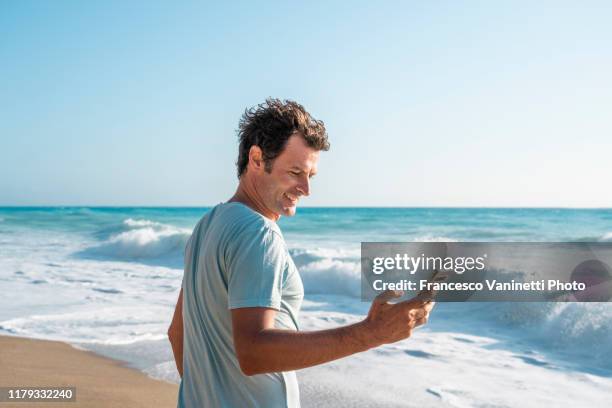 man using the smartphone at the seaside, lefkada, greece. - smartphone strand stock-fotos und bilder