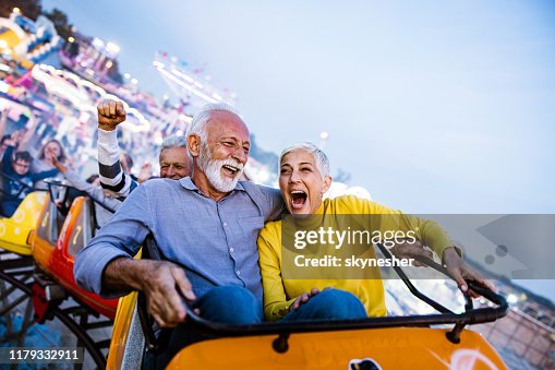 Carefree seniors having fun on rollercoaster at amusement park.