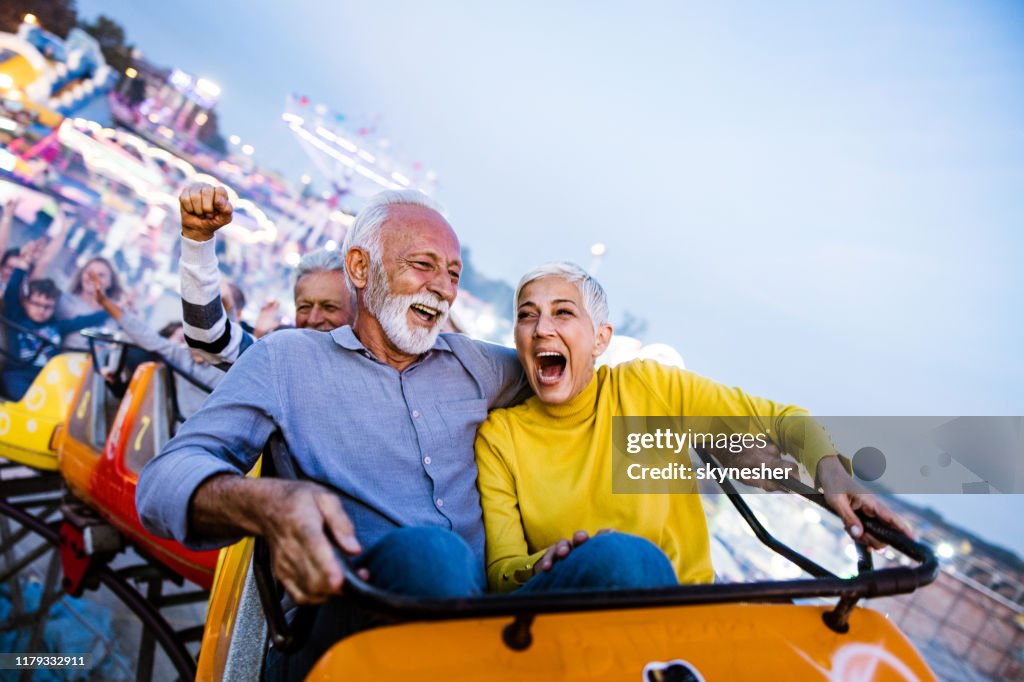 Carefree seniors having fun on rollercoaster at amusement park.