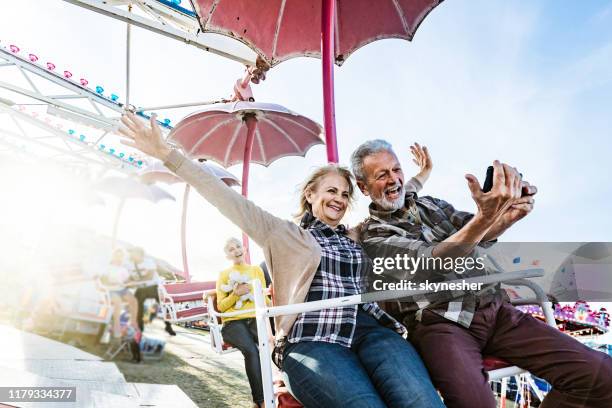 happy senior couple taking a selfie during amusement park ride. - festival selfie stock pictures, royalty-free photos & images