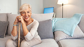 Happy senior woman with walking stick seating at home.