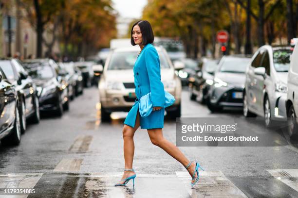 Tiffany Hsu wears a blue oversized jacket dress, a blue bag, blue heels shoes, outside Miu Miu, during Paris Fashion Week - Womenswear Spring Summer...