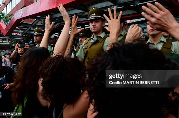 Women dressed in black and wearing eye patches, representing protesters injured with pellets shot by riot police, raise their hands to a line of...