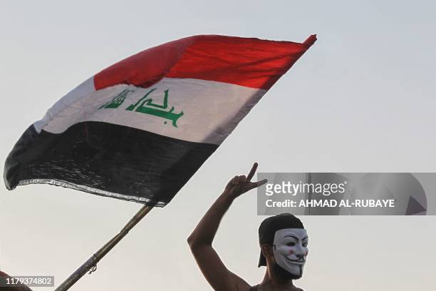 An Iraqi protester, wearing the Guy Fawkes mask, flashes the V for victory sign during ongoing anti-government demonstrations on al-Sinek bridge in...