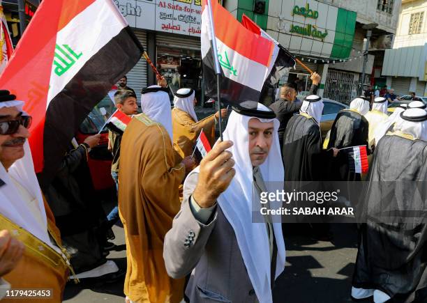 Iraqi protesters, dressed in traditional outfits, wave national flags in the capital Baghdad's Tahrir square during ongoing anti-government...