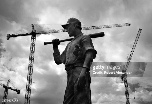 Bronze statue of a baseball player in front of Coors Field is framed by nearby construction cranes in downtown Denver, Colorado. Coors Field is the...