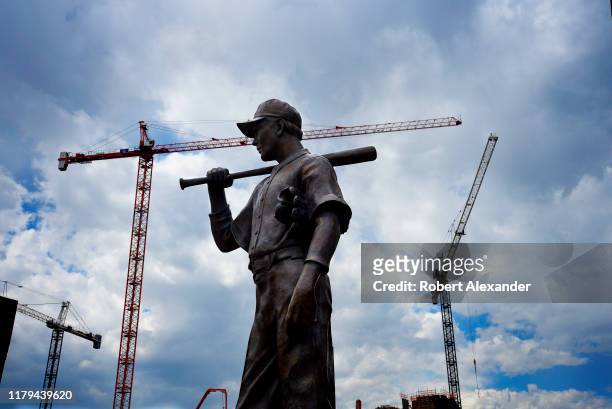 Bronze statue of a baseball player in front of Coors Field is framed by construction cranes at a job site in Denver, Colorado. Coors Field is the...