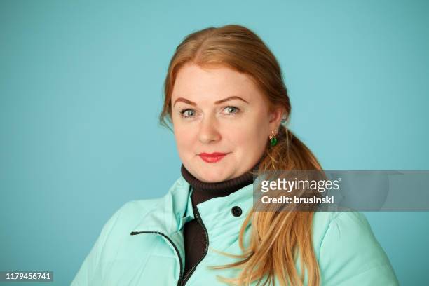 studio portrait of an attractive 35 year old red-haired woman in a blue jacket on a blue background - fat redhead stock pictures, royalty-free photos & images