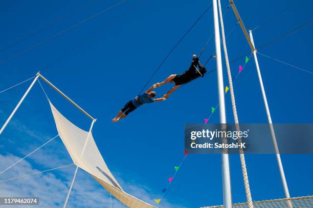 twee trapeze artiesten vliegen in de blauwe hemel - trapezeartiest stockfoto's en -beelden